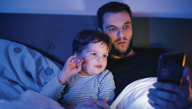 Man holding a baby at night and looking at his phone.