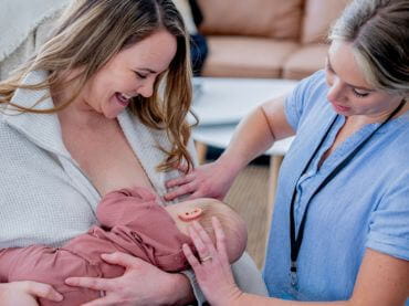 Women breastfeeding a baby with assistance from a doctor.