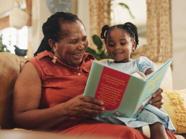 Woman reading a book to a young girl sitting in her lap