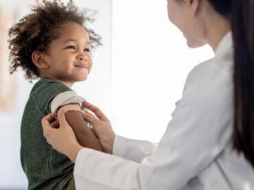 Little boy smiling while he gets a band aid placed on his arm by a doctor