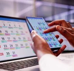 Person on their smartphone in front of a laptop booking an appointment
