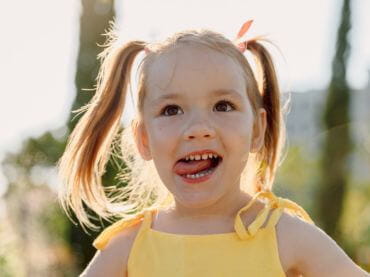 Little girl with ping tails and a yellow tank top sticking her tongue out