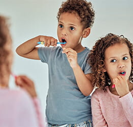 Two kids brushing their teeth in the mirror together