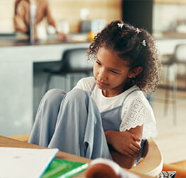 Young girl holding her knees to her chest and looking like she has a stomach ache
