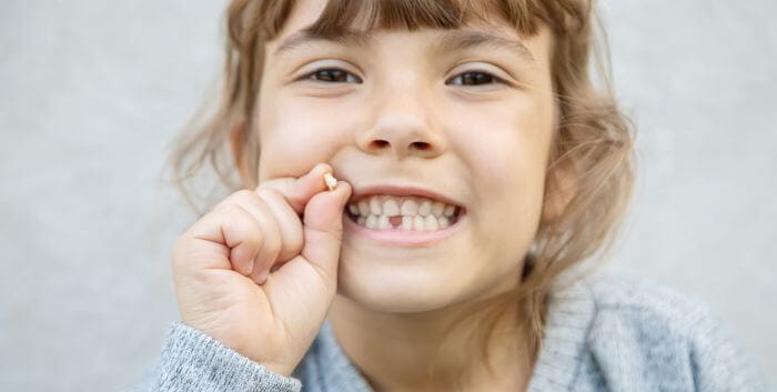 Child with a gap toothed smile holding her lost tooth