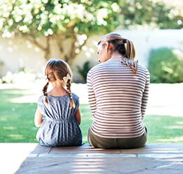 Mom and young daughter sitting together on the front porch talking