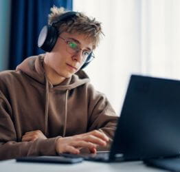 Teen wearing glasses and headphones and using a laptop