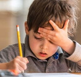 Boy doing schoolwork with his head in his hand