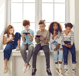 A line of kids sitting in a row playing on their smartphones and tablets