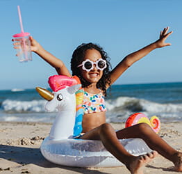 Young girl wearing sunglasses and holding a cup while sitting in a unicorn floatie