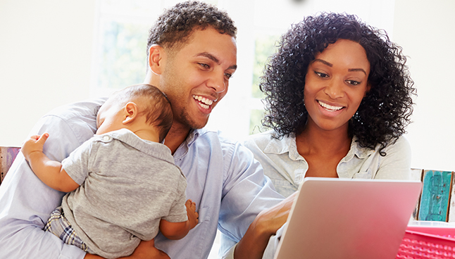 African American couple holding a baby and looking at the computer