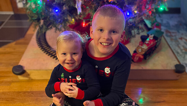 Image of Bethany's children sitting in front of their Christmas tree.