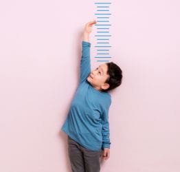 Boy measuring himself against a wall chart
