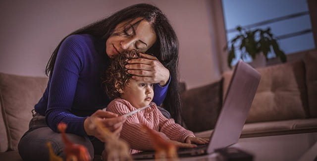 Mom checking her child's temperature while on her laptop
