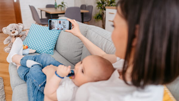 Mom with a baby on a couch talking to a doctor on her mobile phone