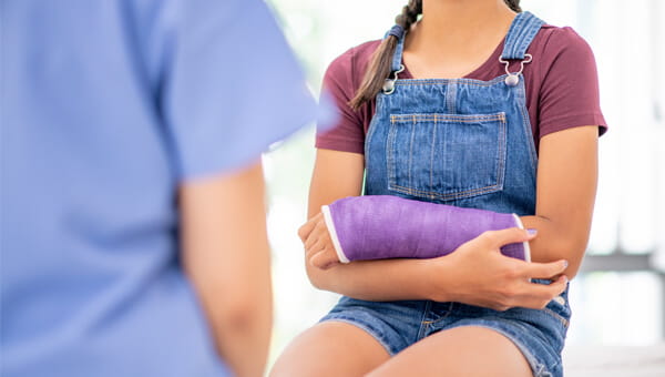 Girl with a purple cast on her arm talking to a healthcare provider