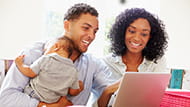 African American couple holding a baby looking at a lap top