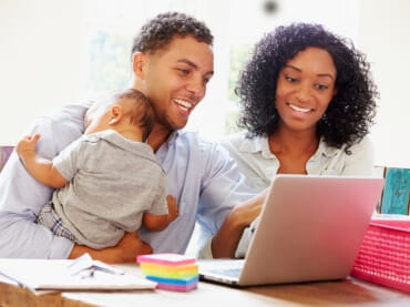 African American couple holding a baby looking at a lap top
