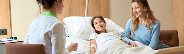 Young girl laying in a hospital bed with her mom next to her, both smiling at a doctor at the bedside
