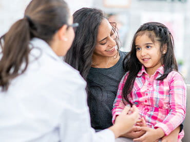 Young child girl sitting in her mom's lap and talking to a doctor