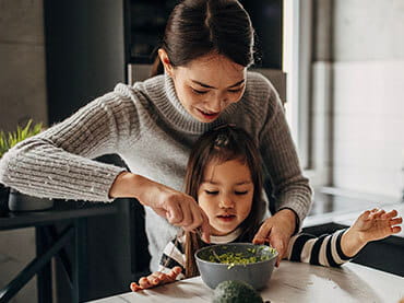 Mom standing over her daughter while they make a salad together