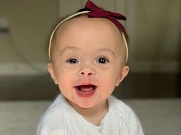 Baby with a red bow on her head looking into the camera and smiling