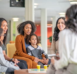 Moms in chairs sitting in a circle, the middle one with a childin her lap