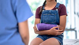 Girl sitting in a doctors office with a purple cast on her arm.