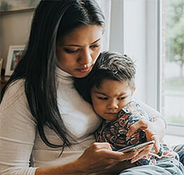 Woman with a son in her lap looking at her phone with concern on her face