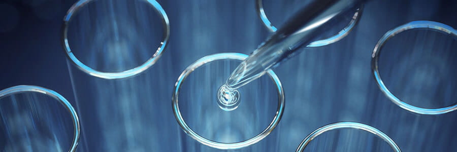 A glass dropper with a drop falling off into a glass tube