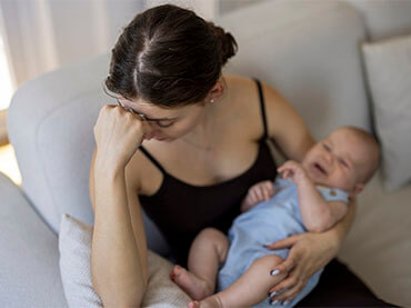 Mother with a baby in her arms and her head in her hand