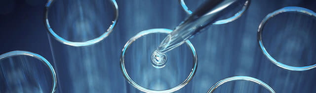 A glass dropper with a drop falling off into a glass tube