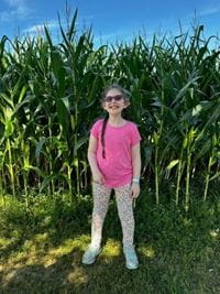 Ella Weisbord in a pink shirt in front of corn