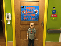 Porter standing in front of a poster with notes and signatures with "Happy Last Chemo Porter" in big letters in the center