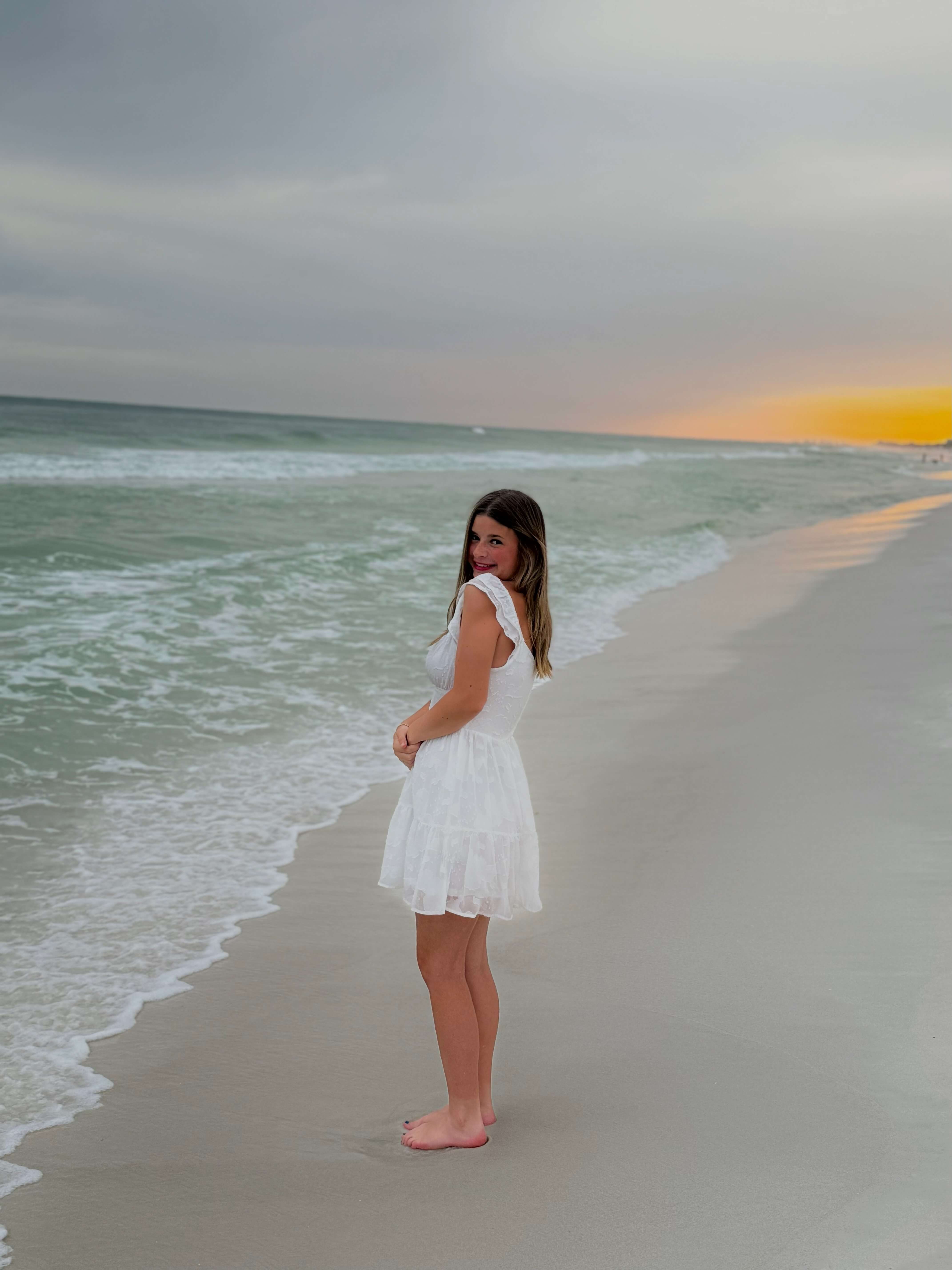 Alaina wearing a white dress and smiling on the beach
