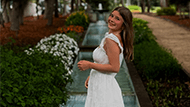 Alaina wearing a white dress and smiling in front of flowers