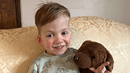A young boy named Ajax, smiling and holding a brown dog stuffed animal