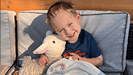 Lorenzo smiling and holding his stuffed animal sheep.
