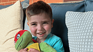 A young boy named Miller smiling and holding a stuffed Teenage Mutant Ninja Turtle