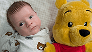 A young baby named Otto laying with a Winnie the Pooh stuffed animal