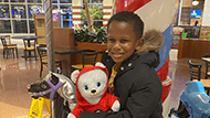 A young boy named Yahya wearing a black winter coat and holding a white bear stuffed animal