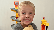 Matthew smiling and holding a teddy bear in front of a toy car track