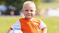 Jaxson Harris in an orange uniform with a soccer ball in his arm