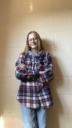 Anna Fleming in a plaid shirt standing in fornt of a wall with her arms crossed