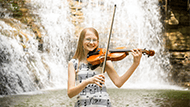 Anna Fleming playing a string instrument in front of a waterfall