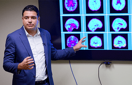 Image of Dr. Pascoal standing in front of brain scans.