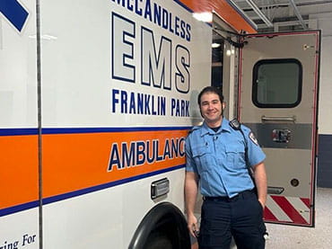 A male EMS leans against an ambulance.