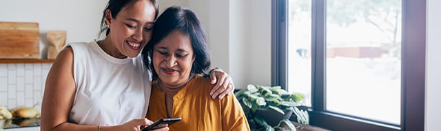 Image of two women hugging while looking at phone.