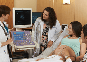 Image of a pregnant woman with three physicians looking at her ultrasound. 