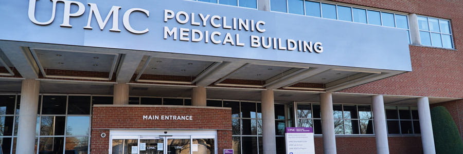 An exterior of the UPMC Polyclinic Medical Building. It is a red brick building with blue tinted windows.